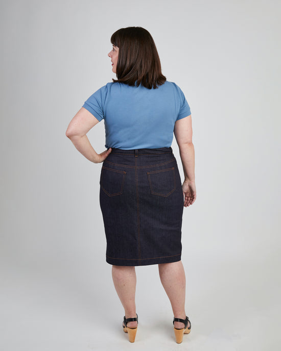Woman wearing a blue t-shirt and dark denim skirt on a plain background. This skirt is the Ellis Denim Skirt sewing pattern from Cashmerette.