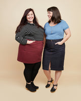 Two women standing side by side against a beige background, wearing skirts and tights. This skirt is the Ellis Denim Skirt sewing pattern from Cashmerette.