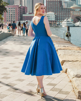 Woman in a blue dress standing by a waterfront with city skyline in the background. This skirt is the Gilmore Circle Skirt sewing pattern from Cashmerette.