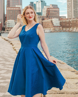 Woman in a blue dress standing by a waterfront with city skyline in the background. This skirt is the Gilmore Circle Skirt sewing pattern from Cashmerette.
