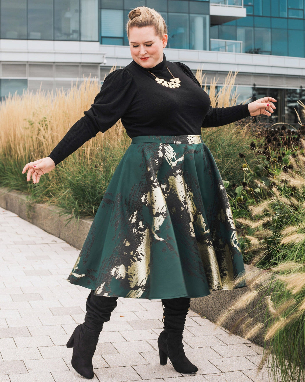 Woman in a black top and green skirt with floral pattern standing outdoors. This skirt is the Gilmore Circle Skirt sewing pattern from Cashmerette.