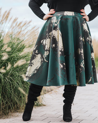 Person wearing a green and black patterned skirt with black boots in an outdoor setting. This skirt is the Gilmore Circle Skirt sewing pattern from Cashmerette.