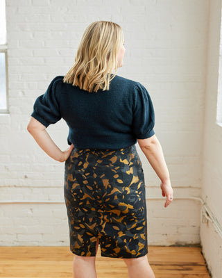 Woman wearing a dark blue top and patterned skirt in a room with white walls and wooden floor. This skirt is the Elmwood Pencil Skirt sewing pattern from Cashmerette.