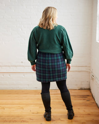 Person wearing a green sweater and plaid skirt standing in a room with wooden floor and white walls. This skirt is the Elmwood Pencil Skirt sewing pattern from Cashmerette.
