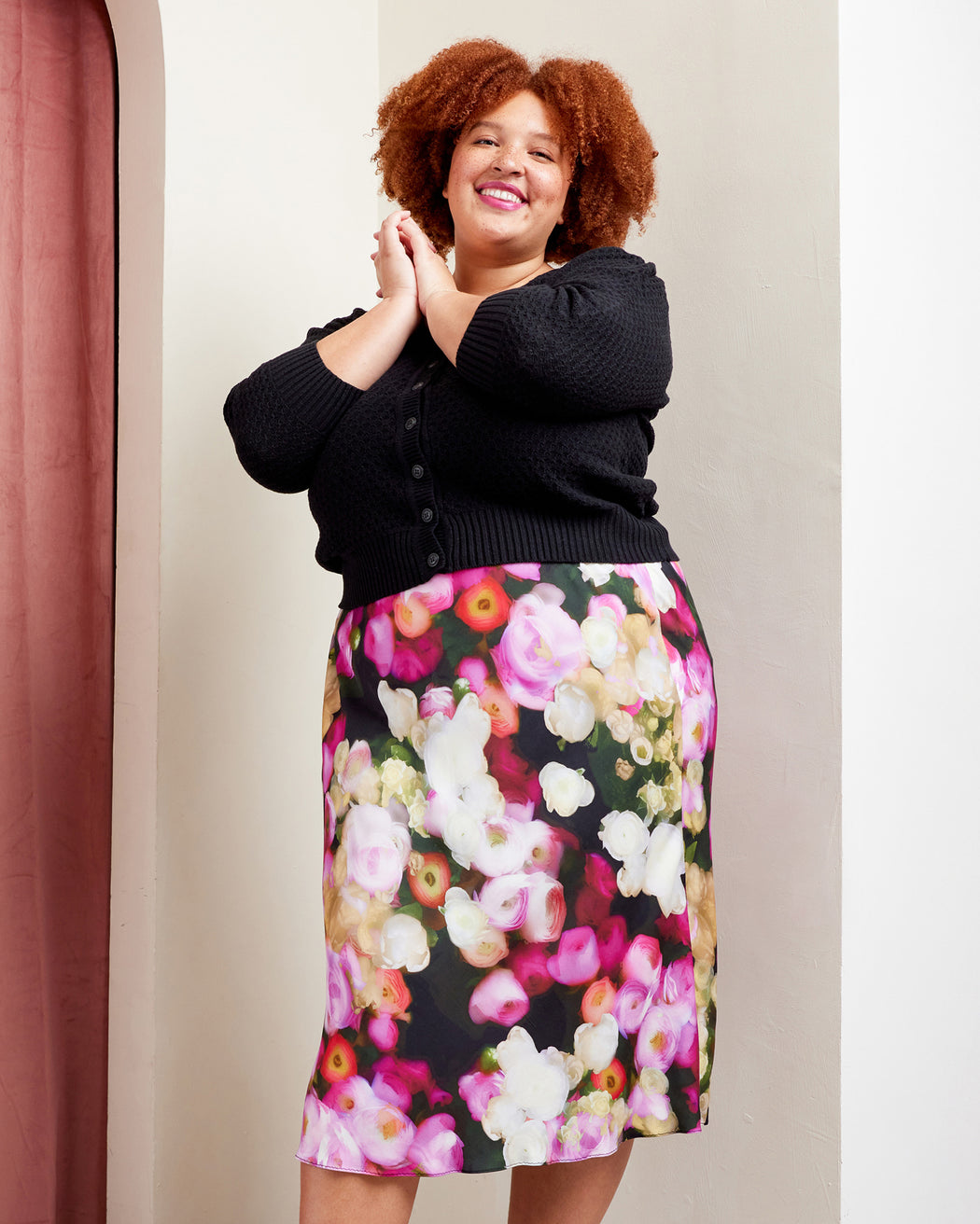 Woman wearing a black cardigan and colorful floral skirt against a neutral background. This skirt is the Astell Bias Skirt sewing pattern from Cashmerette.