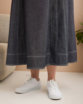 Person wearing a dark denim skirt with white trim and white sneakers on a neutral background. This is the Osgood Skirt sewing pattern from Cashmerette.