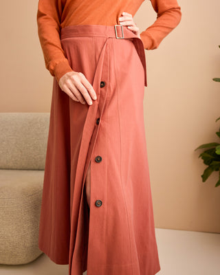 Person wearing an orange sweater and pink skirt with a belt against a beige background.  This is the Osgood Skirt sewing pattern from Cashmerette.