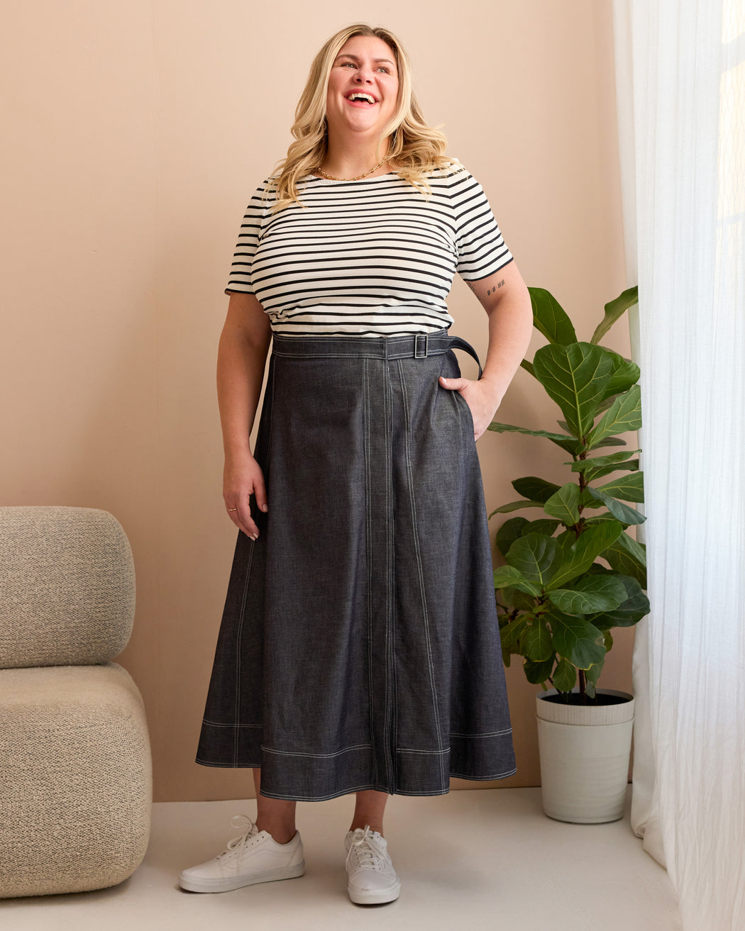 Woman wearing a striped shirt and dark denim skirt standing indoors with a plant and chair in the background. This is the Osgood Skirt sewing pattern from Cashmerette.