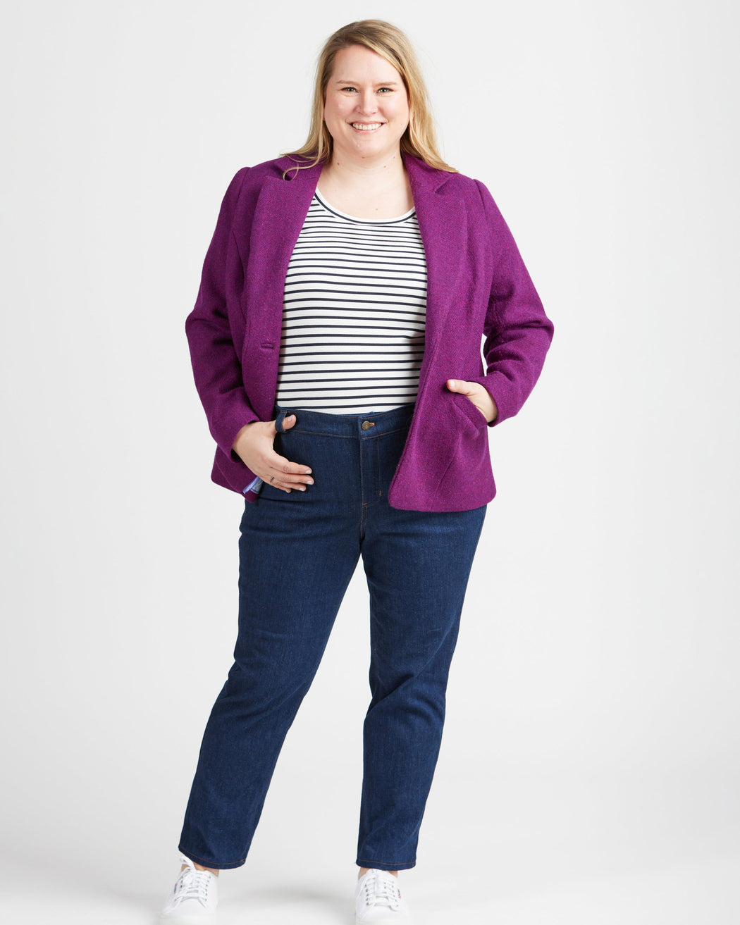 Woman wearing a purple jacket, striped shirt, and blue jeans on a white background. These jeans are the Ames Jeans sewing pattern from Cashmerette.