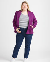 Woman wearing a purple jacket, striped shirt, and blue jeans on a white background. These jeans are the Ames Jeans sewing pattern from Cashmerette.