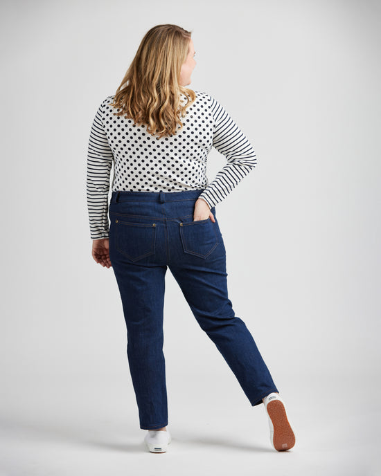 Woman wearing a polka dot top and blue jeans on a plain background. These jeans are the Ames Jeans sewing pattern from Cashmerette.