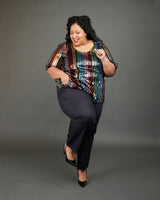 Person wearing a colorful sequin top and black pants on a gray background. These jeans are the Ames Jeans sewing pattern from Cashmerette.