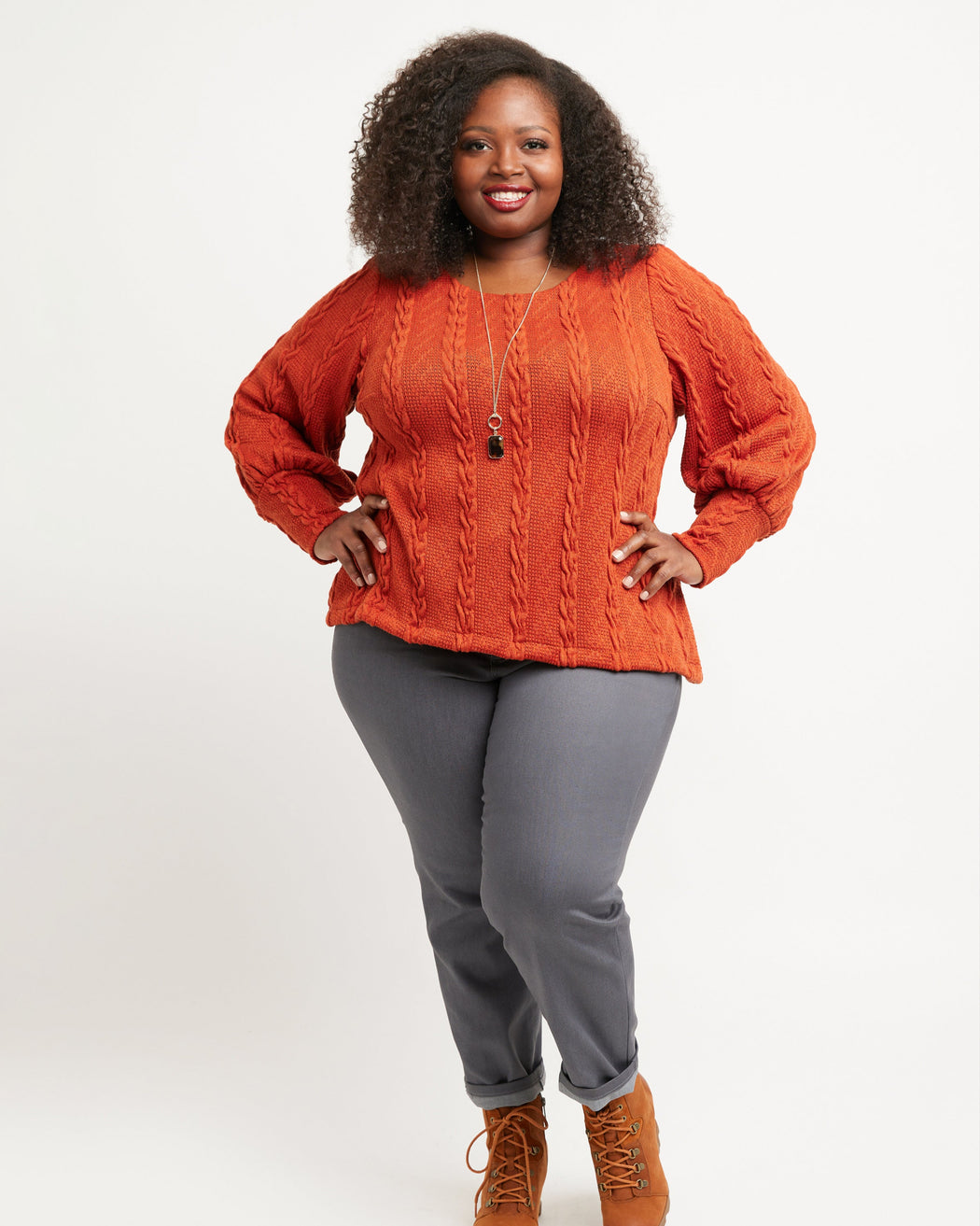 Woman wearing an orange cable knit sweater and gray pants on a white background. These jeans are the Ames Jeans sewing pattern from Cashmerette.