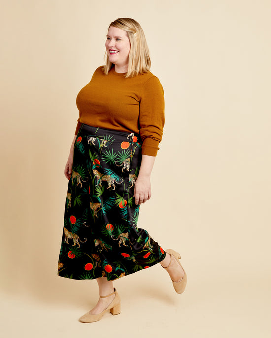 Woman wearing a mustard sweater and patterned skirt on a beige background. These pants are the Calder Pants & Shorts sewing pattern from Cashmerette.