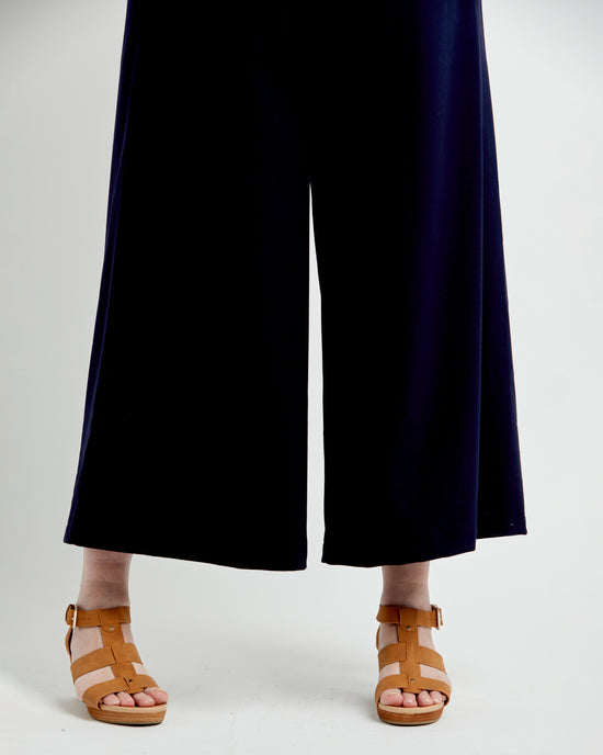 Person wearing navy blue pants and brown sandals on a white background. These pants are the Calder Pants & Shorts sewing pattern from Cashmerette.
