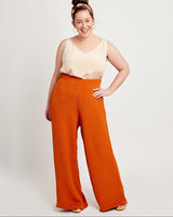 Woman wearing a cream top and orange wide-leg pants on a white background. These pants are the Calder Pants & Shorts sewing pattern from Cashmerette.
