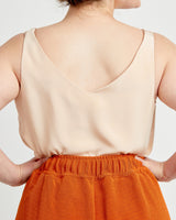 Person wearing a beige sleeveless top and orange pants on a plain background. These pants are the Calder Pants & Shorts sewing pattern from Cashmerette.