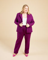 Woman wearing a purple suit on a beige background. These pants are the Meriam Trousers sewing pattern from Cashmerette.