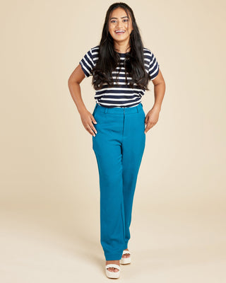 Woman wearing a striped shirt and blue pants on a beige background. These pants are the Meriam Trousers sewing pattern from Cashmerette.