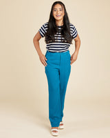 Woman wearing a striped shirt and blue pants on a beige background. These pants are the Meriam Trousers sewing pattern from Cashmerette.
