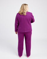 Person wearing a purple outfit on a white background. These pants are the Meriam Trousers sewing pattern from Cashmerette.
