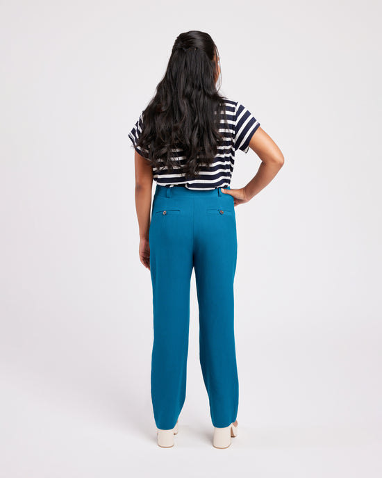 Person wearing blue pants and a striped shirt on a white background. These pants are the Meriam Trousers sewing pattern from Cashmerette.