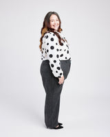 Woman wearing a polka dot blouse and gray pants on a white background. These pants are the Meriam Trousers sewing pattern from Cashmerette.