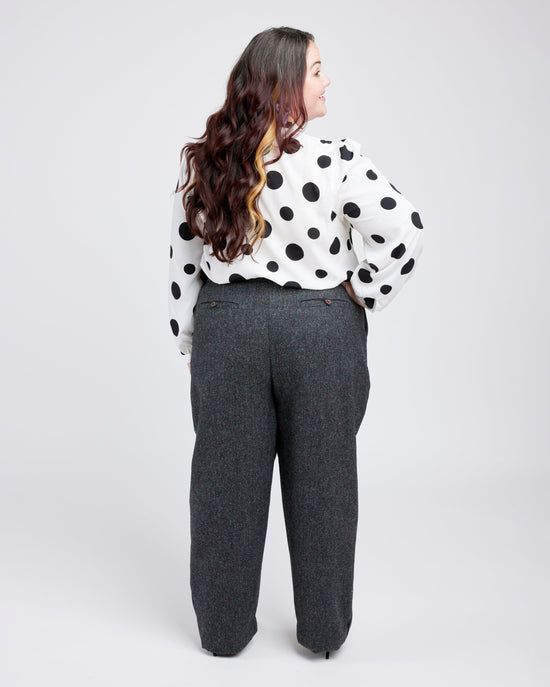 Person wearing a polka dot blouse and gray pants on a white background. These pants are the Meriam Trousers sewing pattern from Cashmerette.