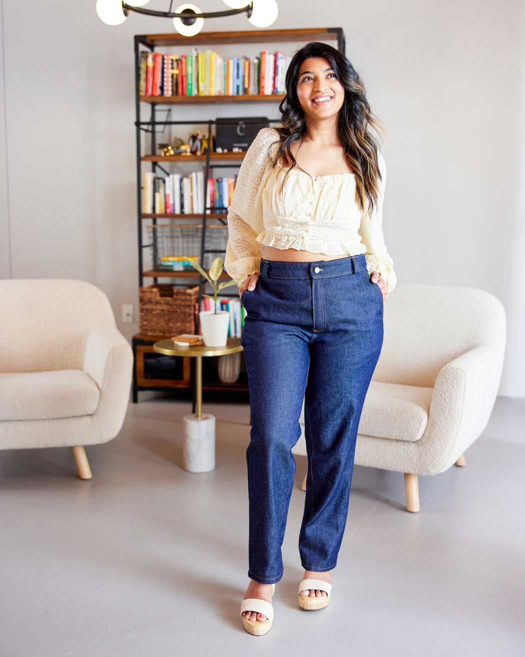 Woman in a living room wearing a yellow top and blue jeans. These jeans are the Creston Jeans sewing pattern from Cashmerette.