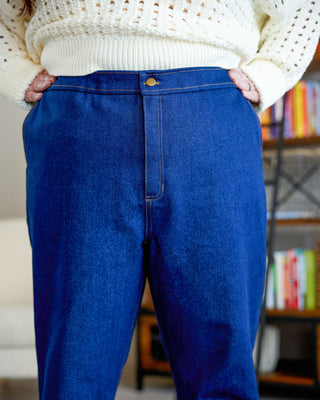 Person wearing blue jeans and a white sweater in a casual setting with books in the background. These jeans are the Creston Jeans sewing pattern from Cashmerette.