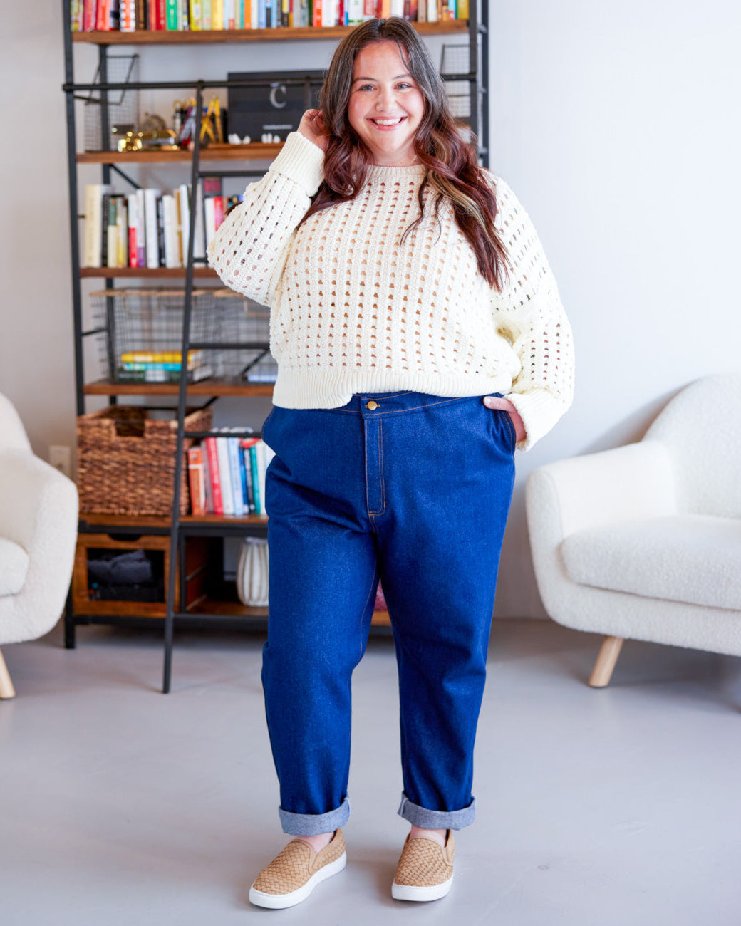 Woman wearing a white sweater and blue pants standing in a living room. These jeans are the Creston Jeans sewing pattern from Cashmerette.
