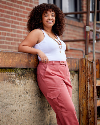 Woman in white tank top and pink pants leaning against a brick wall. These pants are the Esmond Cargo Pants sewing pattern from Cashmerette.