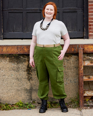 Person wearing a light gray shirt, green cargo pants, and black boots standing against a textured wall. These pants are the Esmond Cargo Pants sewing pattern from Cashmerette.