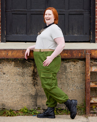 Person wearing a light gray shirt and green cargo pants leaning against a wall. These pants are the Esmond Cargo Pants sewing pattern from Cashmerette.