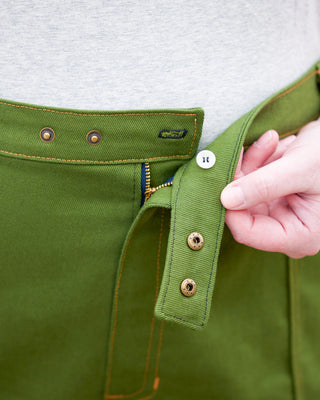 Close-up of a green pants with gold buttons, and a hand adjusting the waistband. These pants are the Esmond Cargo Pants sewing pattern from Cashmerette.