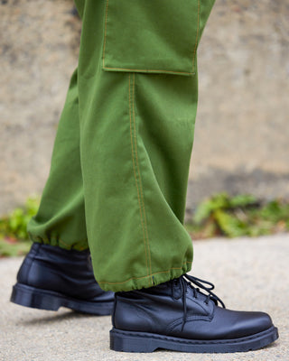 Person wearing green pants and black boots on a blurred outdoor background. These pants are the Esmond Cargo Pants sewing pattern from Cashmerette.