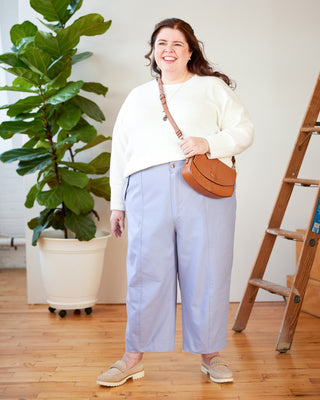 Woman in a white sweater and light blue pants holding a brown leather bag indoors. These pants are the Vinton Pants sewing pattern from Cashmerette.