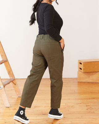 Person wearing olive green pants and black sneakers on a wooden floor. These pants are the Vinton Pants sewing pattern from Cashmerette.
