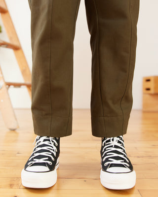 Person wearing brown pants and black high-top sneakers on a wooden floor. These pants are the Vinton Pants sewing pattern from Cashmerette.