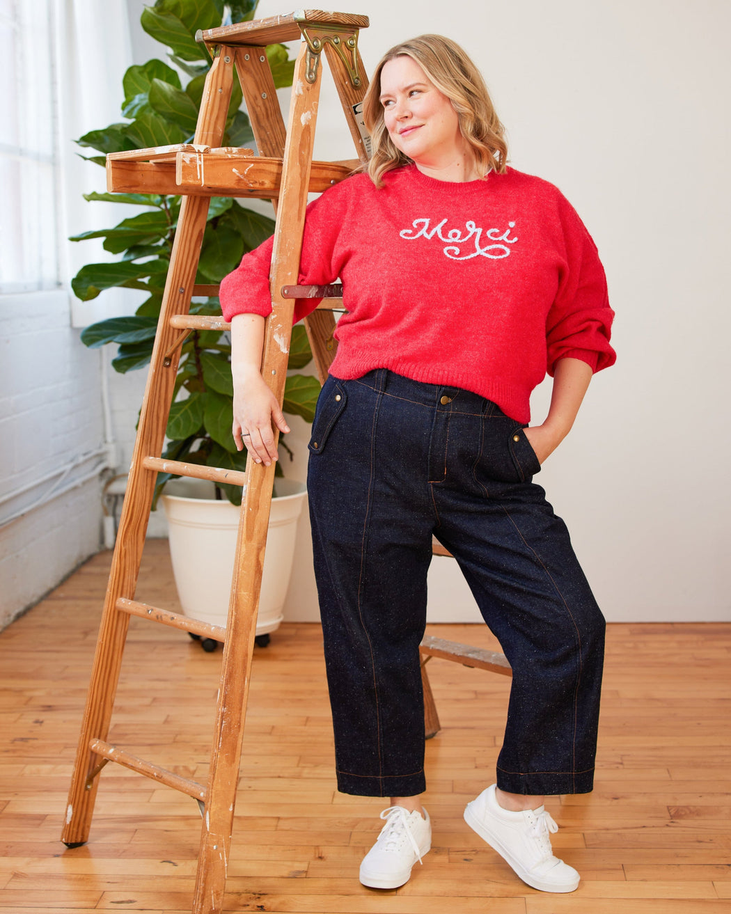 Woman in a red sweater standing next to a wooden ladder indoors. These pants are the Vinton Pants sewing pattern from Cashmerette.
