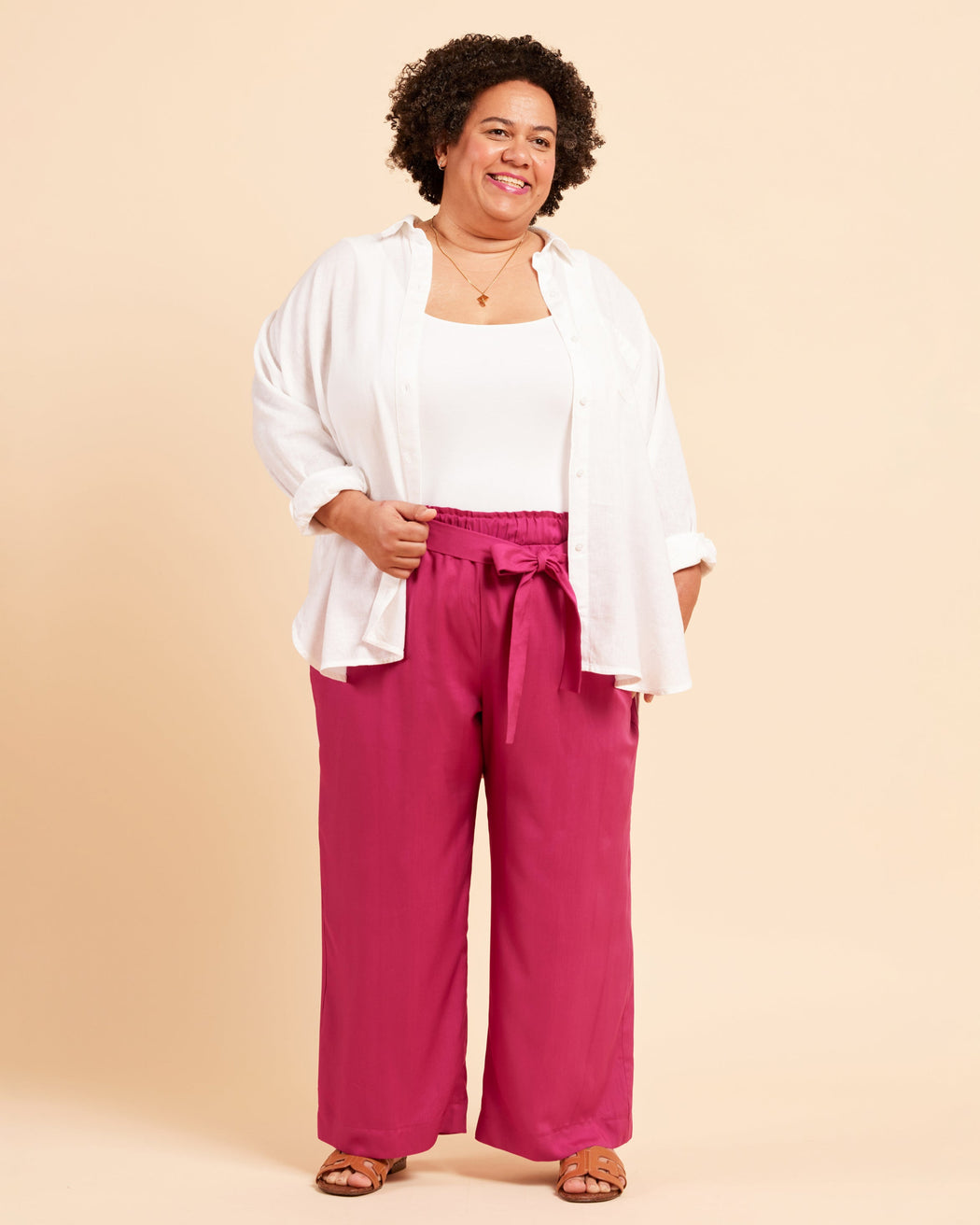 Woman wearing a white top and pink pants against a beige background. These pants are the Everett Pants & Shorts sewing pattern from Cashmerette.
