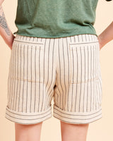Beige shorts with black stripes worn by a person on a beige background. These shorts are the Everett Pants & Shorts sewing pattern from Cashmerette.