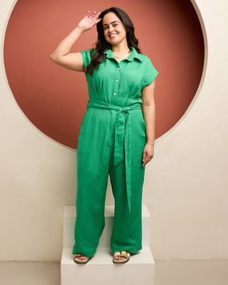 Woman wearing a green jumpsuit standing against a red and beige wall. This is the Roslindale Jumpsuit sewing pattern from Cashmerette.