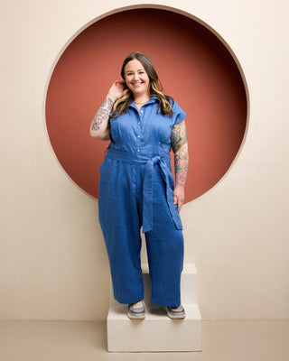 Woman wearing a blue jumpsuit standing in front of a circular red wall. This is the Roslindale Jumpsuit sewing pattern from Cashmerette.