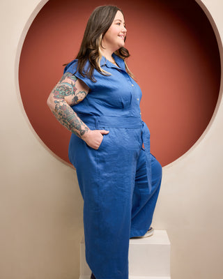 Woman wearing a blue jumpsuit standing against a red circular wall. This is the Roslindale Jumpsuit sewing pattern from Cashmerette.
