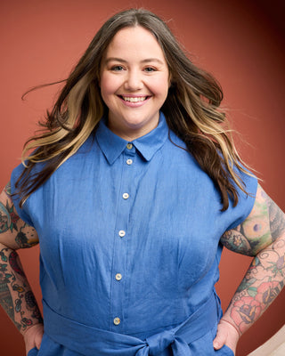 Person wearing a blue sleeveless jumpsuit with a red background. This is the Roslindale Jumpsuit sewing pattern from Cashmerette.