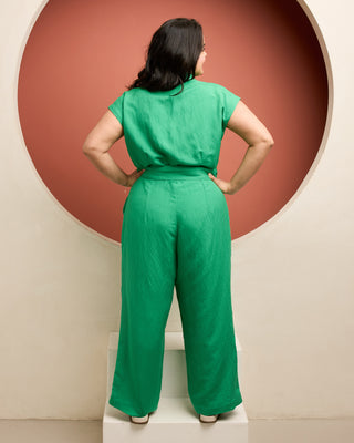 Woman wearing a green jumpsuit standing in front of a circular red and beige wall. This is the Roslindale Jumpsuit sewing pattern from Cashmerette.