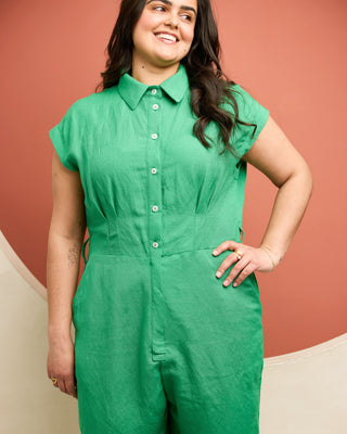 Woman wearing a green jumpsuit against a red-brown background. This is the Roslindale Jumpsuit sewing pattern from Cashmerette.