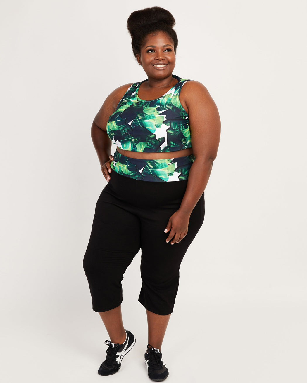Person wearing a green and black leaf-patterned crop top and black capri pants on a white background. These leggings are the Belmont Leggings and Yoga Pants sewing pattern from Cashmerette.