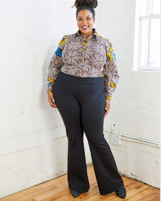 Woman wearing a patterned shirt and black pants standing against a white wall. These pants are the Ashwood Pants sewing pattern from Cashmerette.